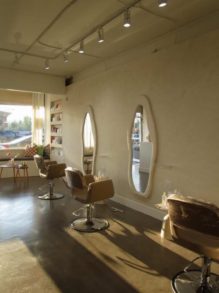 Cream-walled hair salon with oval mirrors, brown styling chairs, and polished concrete flooring
