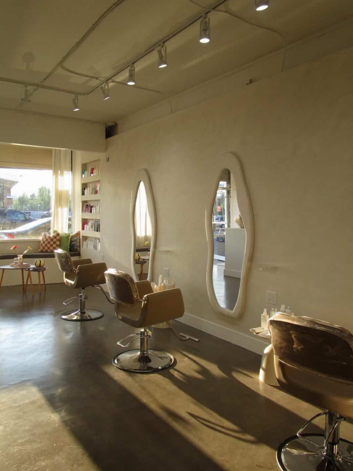 Cream-walled hair salon with oval mirrors, brown styling chairs, and polished concrete flooring