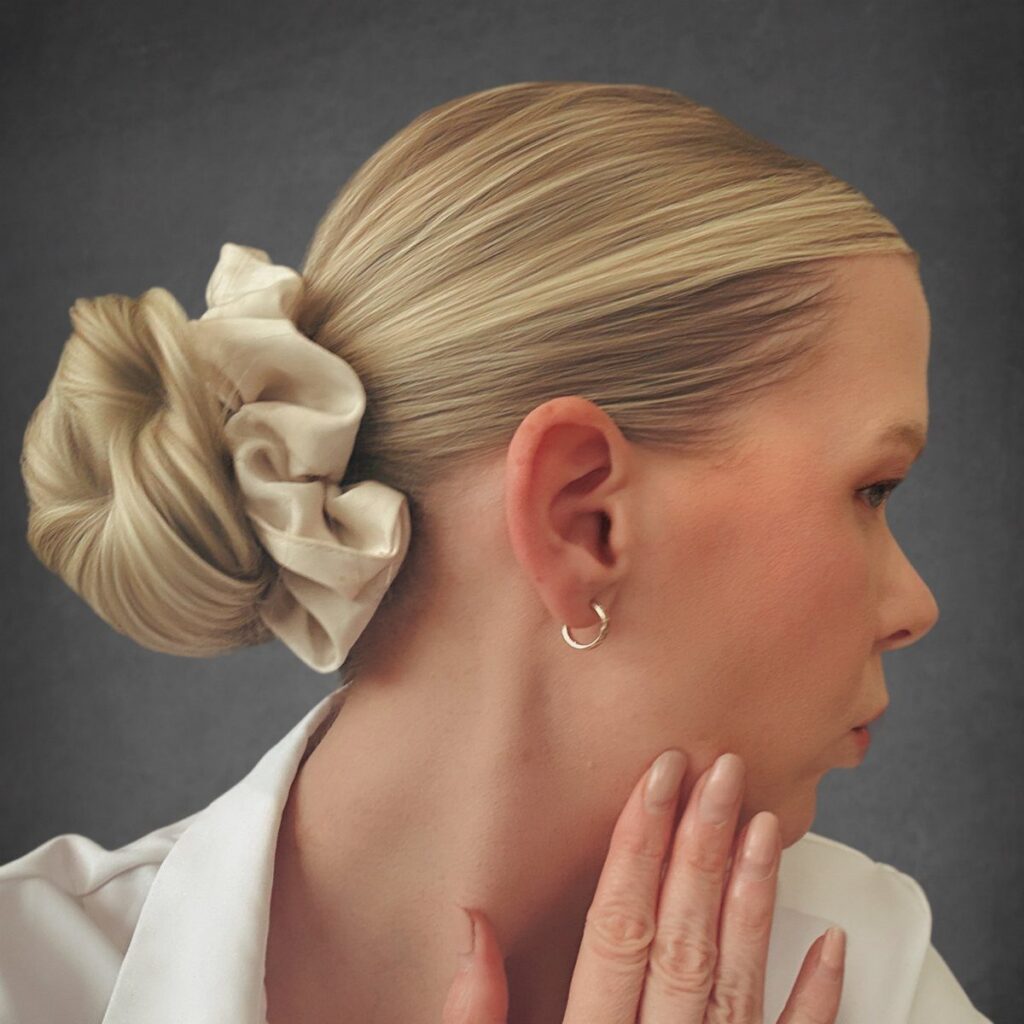 Blonde woman with sleek hair gathered into a low bun and cream scrunchie