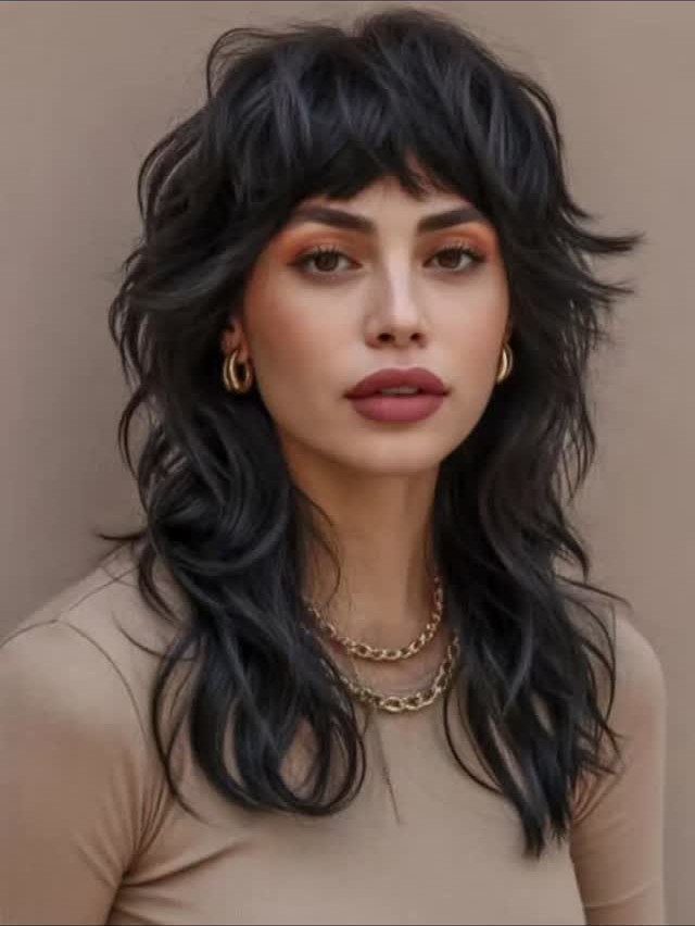 Woman with dark shaggy layers and short bangs against a beige background