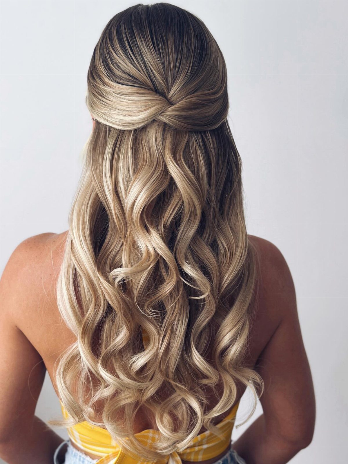 Half-up twisted hairstyle with long cascading blonde curls viewed from behind