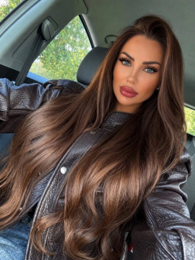 Woman with long, wavy dark brown hair sitting in a car