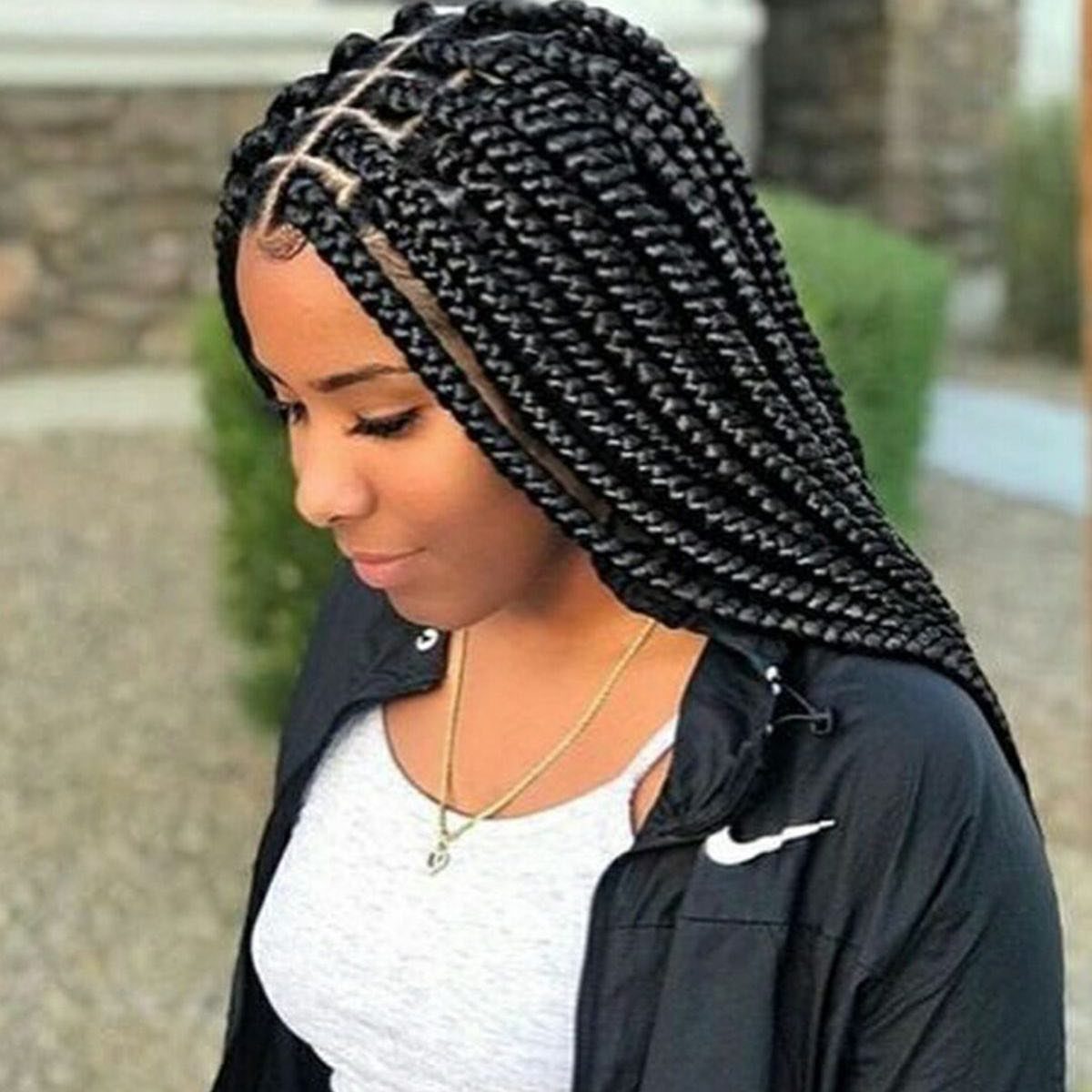 Long black box braids cascade over a woman's shoulder outdoors