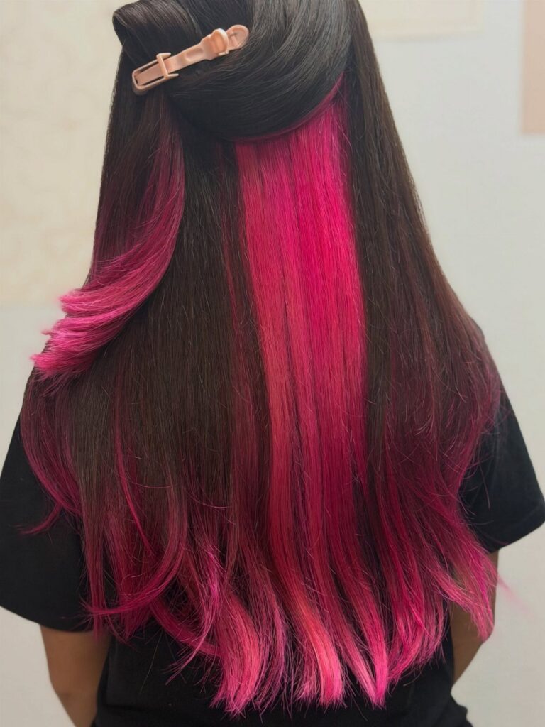 Long dark hair reveals vivid pink peekaboo sections beneath clipped upper layers