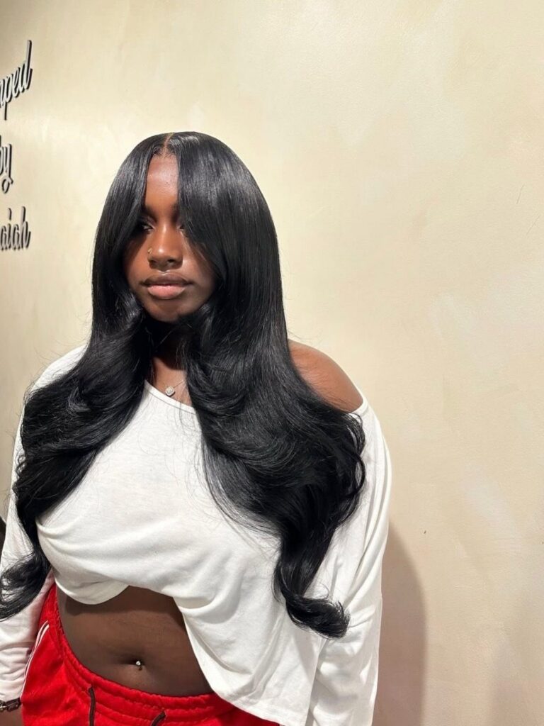 Woman with long, glossy black hair styled in a textured middle part and waves
